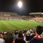 Wide shot of a soccer game in a packed stadium at night.