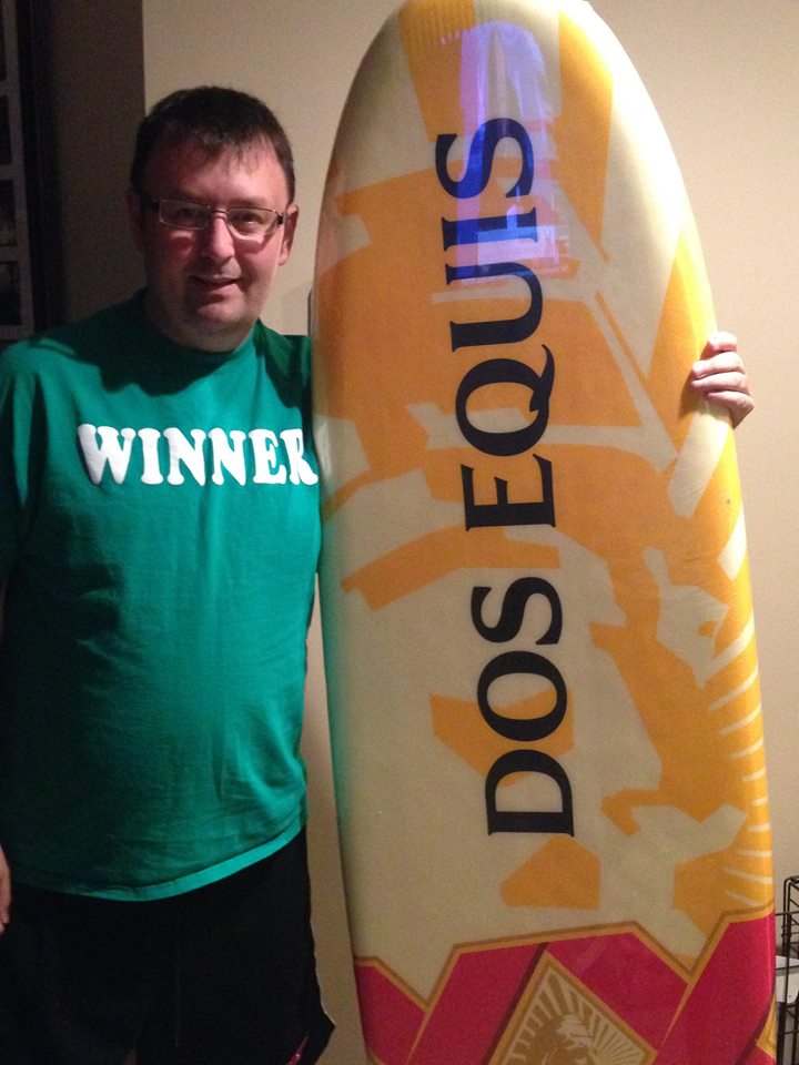 Tom Cavalli posing next to surfboard that says Dos Equis.