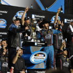Austin Dillon and Advocare team celebrating win at NASCAR Championship around a trophy.
