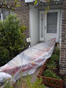 A canoe wrapped in plastic and placed in front of a front door.