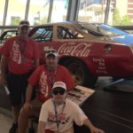 Tom Cavalli and two friends posing in front of race car at Nascar Hall of Fame